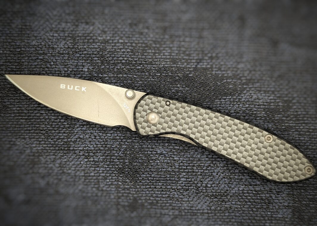 Couteau pliant ouvert Nobleman Carbone de Buck Vue du côté gauche. On voit le poinçon sur la lame. Le manche est en fibre de carbone tressée noire. Couteau industriel de marque américaine Coutellerie Châteauneuf-du-Pape, Coutellerie du Pape, Vaucluse