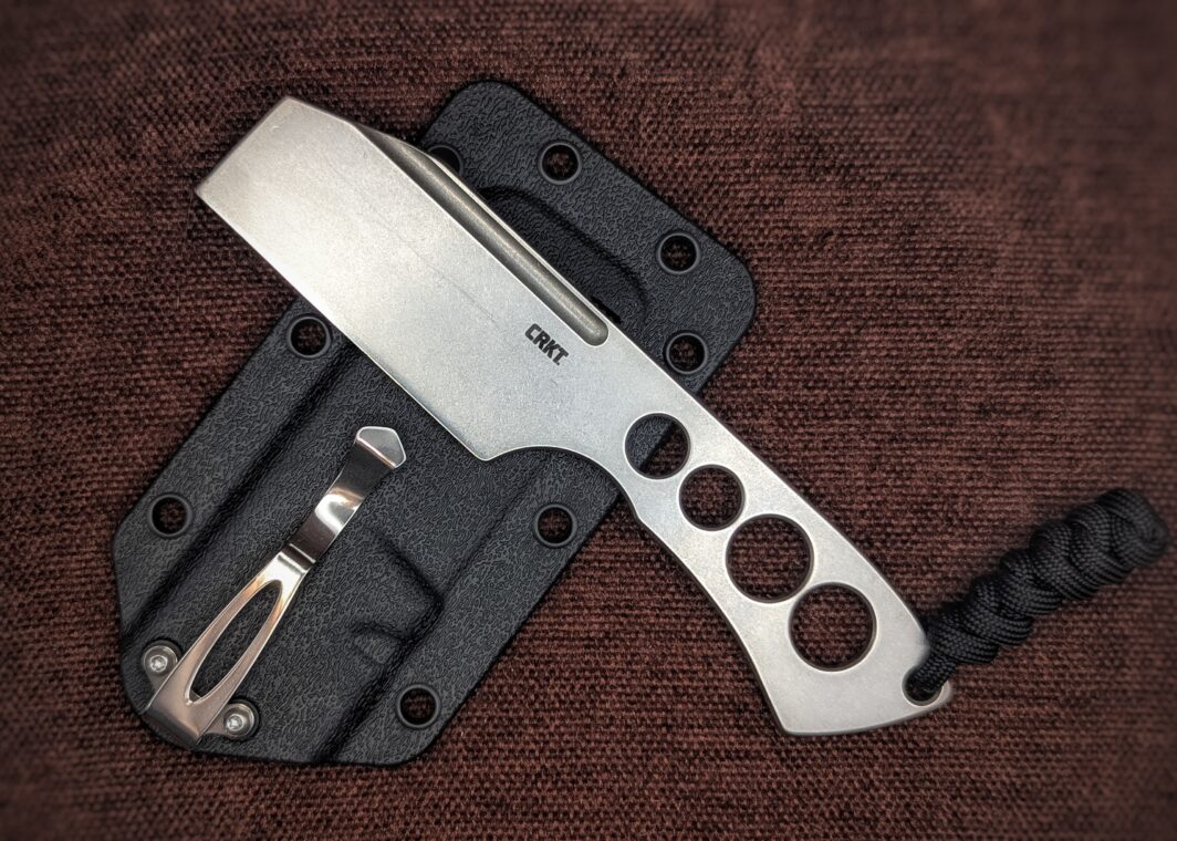 Couteau Razel Chizel de CRKT. Un intégral en acier avec des trous dans le manche. Vue du côté gauche avec le poinçon sur la lame. L'étui avec clip pour la ceinture est en fond. Couteau industriel de marque américaine Coutellerie Châteauneuf-du-Pape, Coutellerie du Pape, Vaucluse