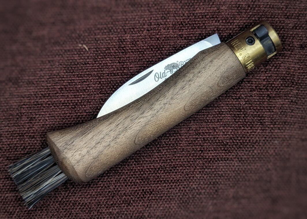 Couteau à champignon OldBear. Manche en noyer. Vue du couteau fermé, on voit le poinçon dépassé. Il y a des poils au bout du manche pour nettoyer les champignons. Couteau industriel de marque italienne Coutellerie Châteauneuf-du-Pape, Coutellerie du Pape, Vaucluse