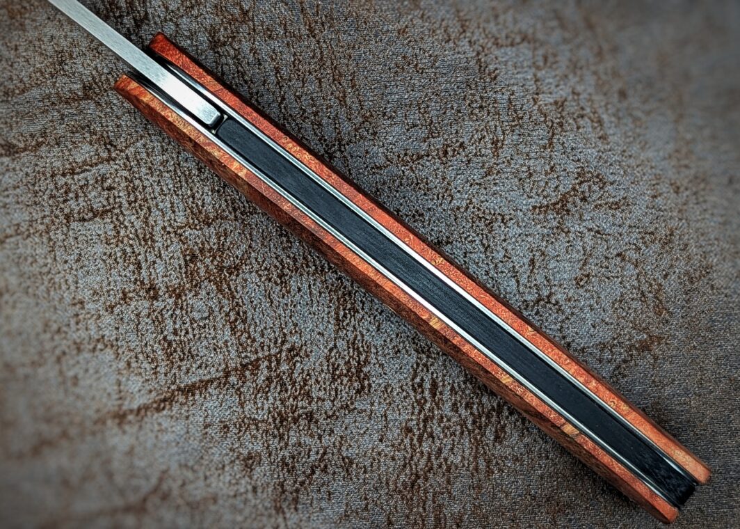 Couteau pliant Gourmet de Maserin. Position ouverte, vue du dessus du couteau. Le manche est en loupe d'érable stabilisée et teintée rouge Couteau industriel de marque italienne Coutellerie Châteauneuf-du-Pape, Coutellerie du Pape, Vaucluse