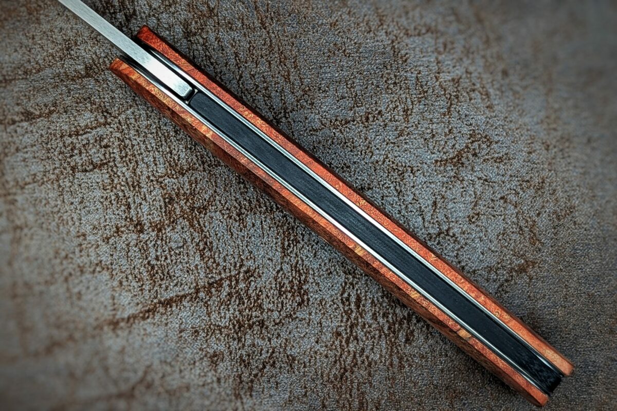 Couteau pliant Gourmet de Maserin. Position ouverte, vue du dessus du couteau. Le manche est en loupe d'érable stabilisée et teintée rouge Couteau industriel de marque italienne Coutellerie Châteauneuf-du-Pape, Coutellerie du Pape, Vaucluse
