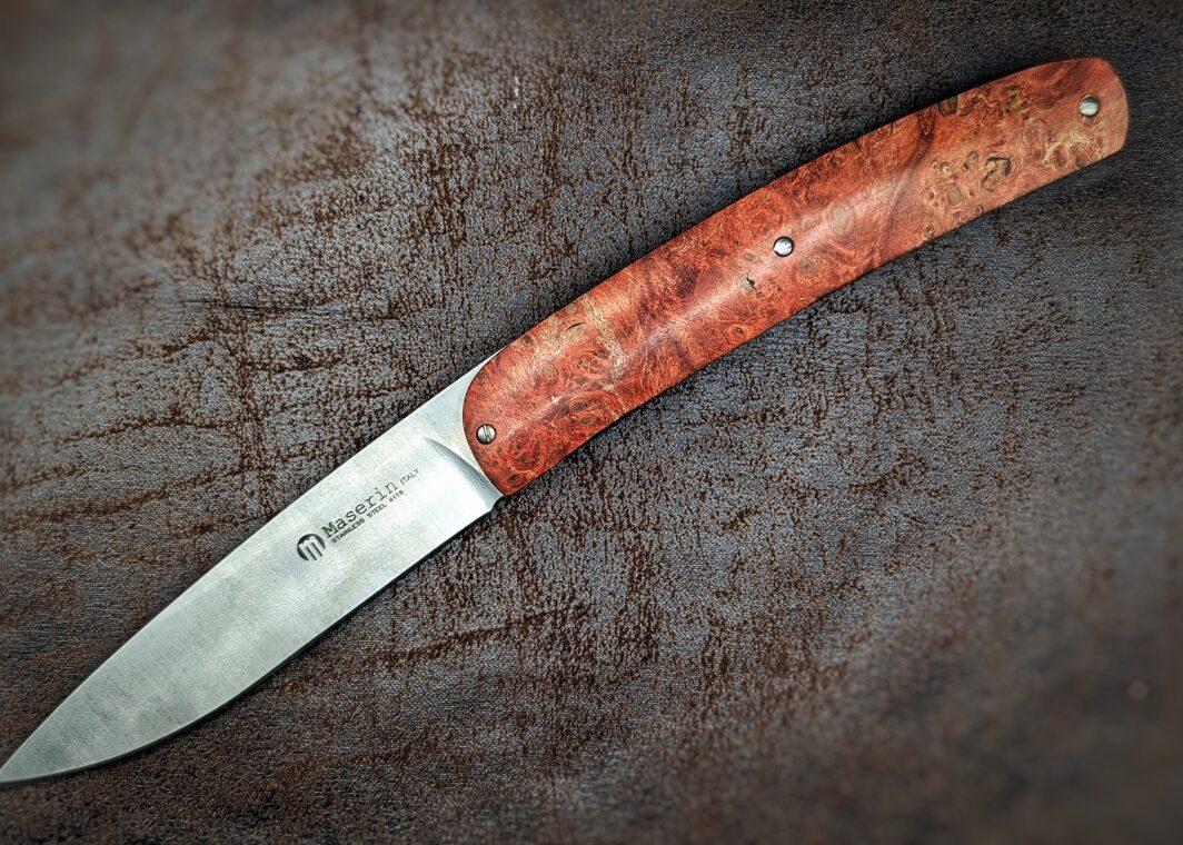 Couteau pliant Gourmet de Maserin. Position ouverte, vue côté gauche du couteau. Le manche est en loupe d'érable stabilisée et teintée rouge. Le poinçon de la marque est sur la lame. Couteau industriel de marque italienne Coutellerie Châteauneuf-du-Pape, Coutellerie du Pape, Vaucluse