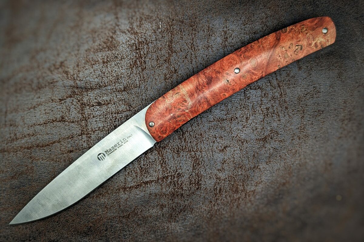 Couteau pliant Gourmet de Maserin. Position ouverte, vue côté gauche du couteau. Le manche est en loupe d'érable stabilisée et teintée rouge. Le poinçon de la marque est sur la lame. Couteau industriel de marque italienne Coutellerie Châteauneuf-du-Pape, Coutellerie du Pape, Vaucluse