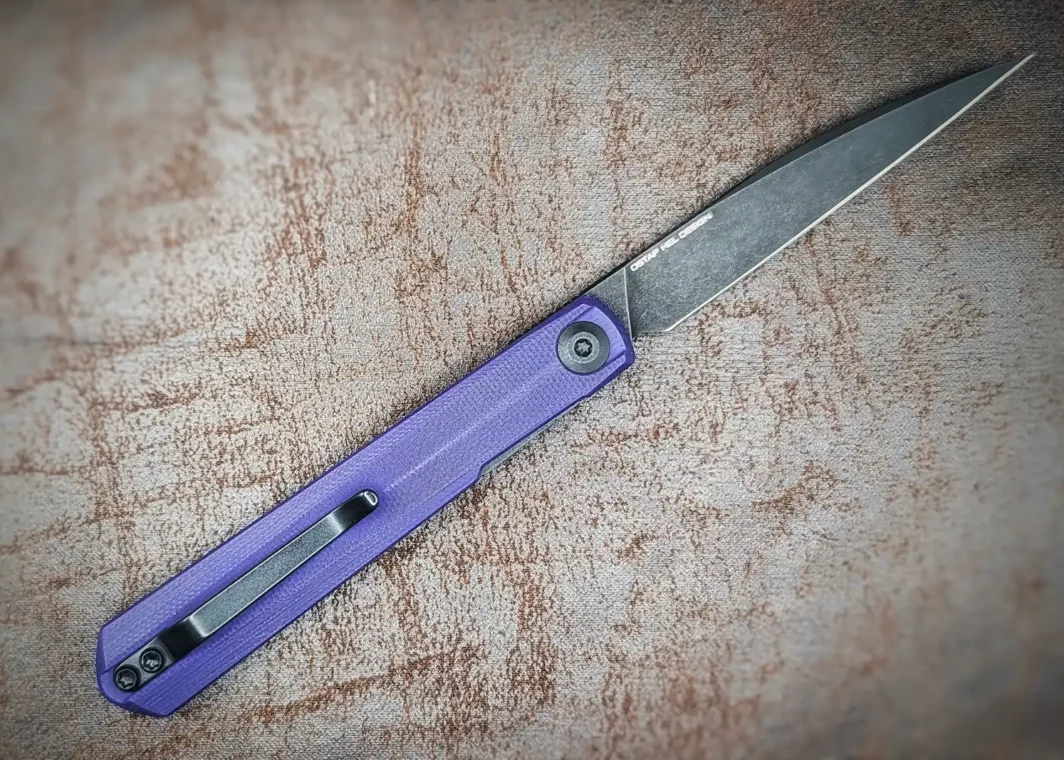 Couteau pliant Clavi de Civivi. Vue côté droit. Position ouverte. La lame est noire, le manche est violet. On aperçoit un clip noir pour accrocher à la ceinture ou à la poche. Couteau industriel Coutellerie Châteauneuf-du-Pape, Coutellerie du Pape, Vaucluse