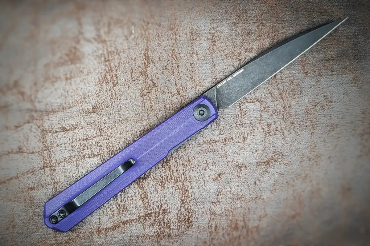 Couteau pliant Clavi de Civivi. Vue côté droit. Position ouverte. La lame est noire, le manche est violet. On aperçoit un clip noir pour accrocher à la ceinture ou à la poche. Couteau industriel Coutellerie Châteauneuf-du-Pape, Coutellerie du Pape, Vaucluse