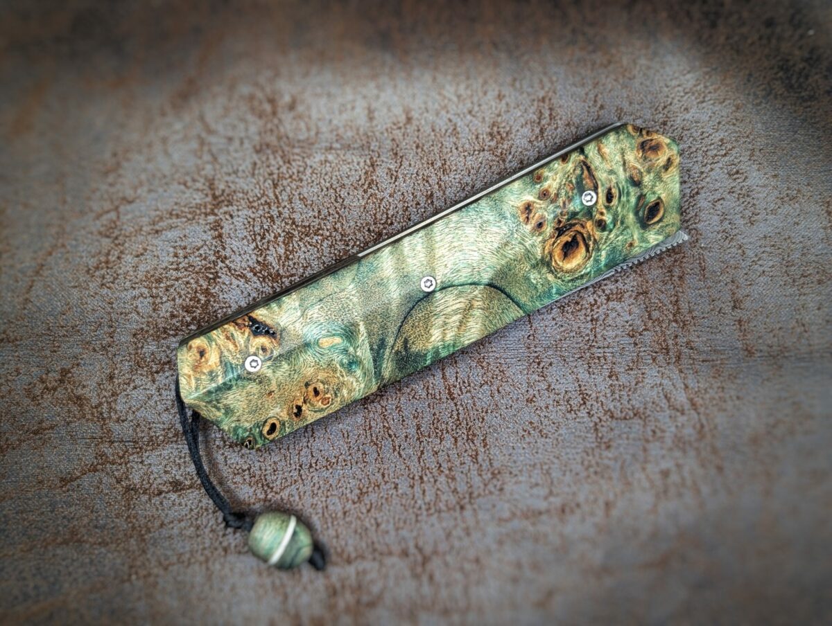 Couteau pliant Liner Lock 'Kiru' de l'artisan Noki. Position fermée, côté droit. Lame en damas 208 couches. Manche en Loupe de peuplier stabilisée teintée vert. Couteau artisanal français à Châteauneuf-du-Pape, Coutellerie du Pape, Vaucluse