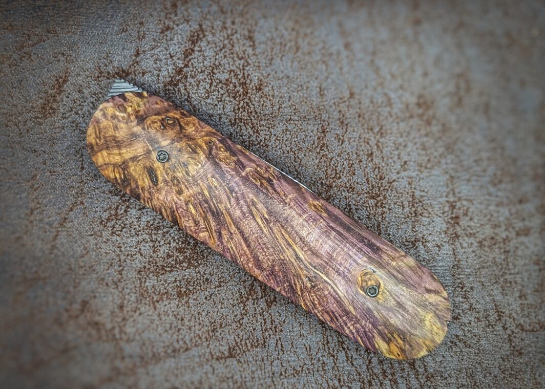 Couteau Le Baldo par l'artisan Noki. Pliant LinerLock FrontFlip. Position fermée, côté droit. Le manche est en bouleau madré stabilisé et teinté violet. Couteau artisanal français à Châteauneuf-du-Pape, Vaucluse Coutellerie du Pape
