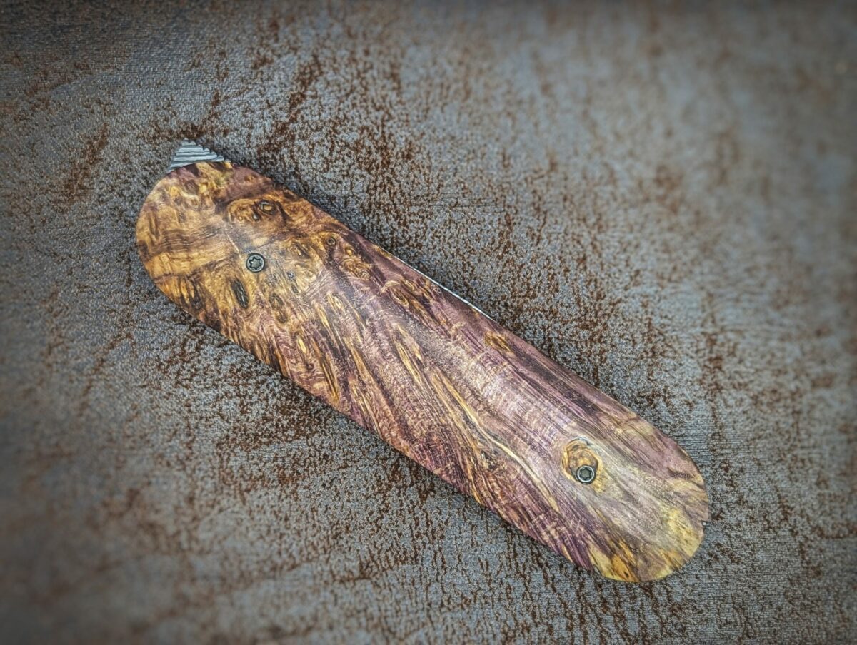 Couteau Le Baldo par l'artisan Noki. Pliant LinerLock FrontFlip. Position fermée, côté droit. Le manche est en bouleau madré stabilisé et teinté violet. Couteau artisanal français à Châteauneuf-du-Pape, Vaucluse Coutellerie du Pape