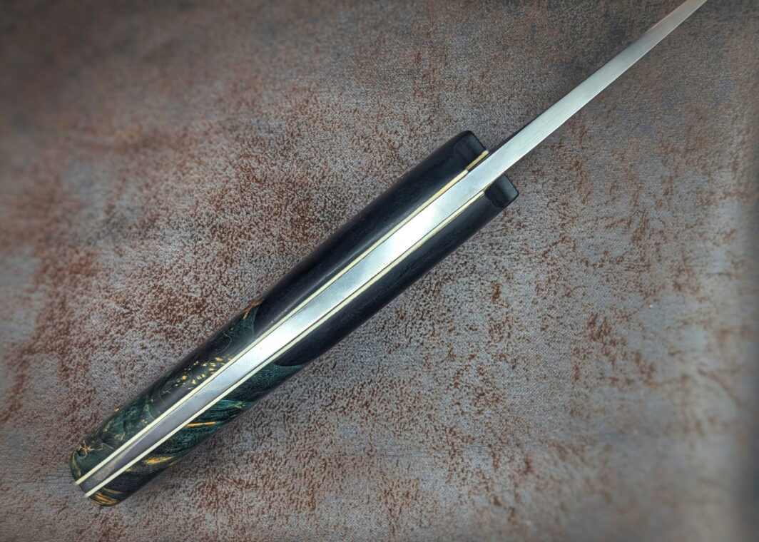 Couteau fixe de l'artisan Lou Marius. Vue du dessus. On voit les intercalaires blancs sur lesquels sont collés les matériaux du manche. Le manche s'affine vers l'arrière du couteau. Couteau artisanal, coutellerie français à Châteauneuf-du-Pape, Vaucluse Coutellerie du Pape