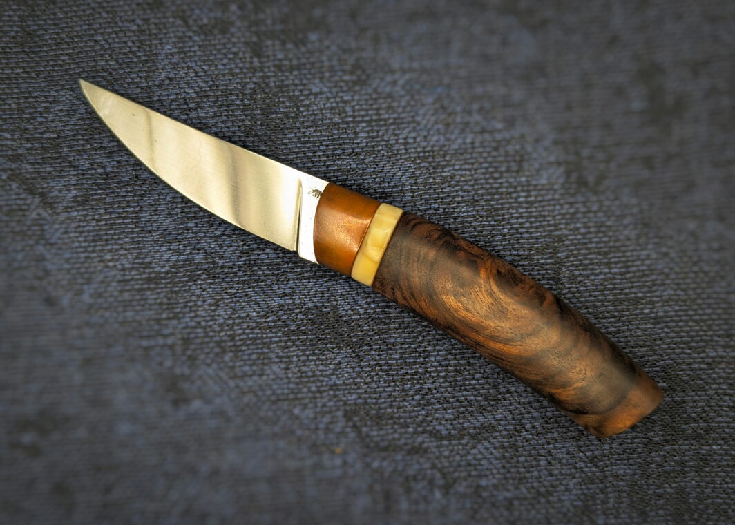 Couteau fixe de l'artisan Lou Marius. Vue du côté gauche. La lame est en finition polie. Le manche est en noyer avec une bague en ivoire de phacochère et une autre en bronze cuivré. Couteau artisanal, coutellerie français à Châteauneuf-du-Pape, Vaucluse Coutellerie du Pape