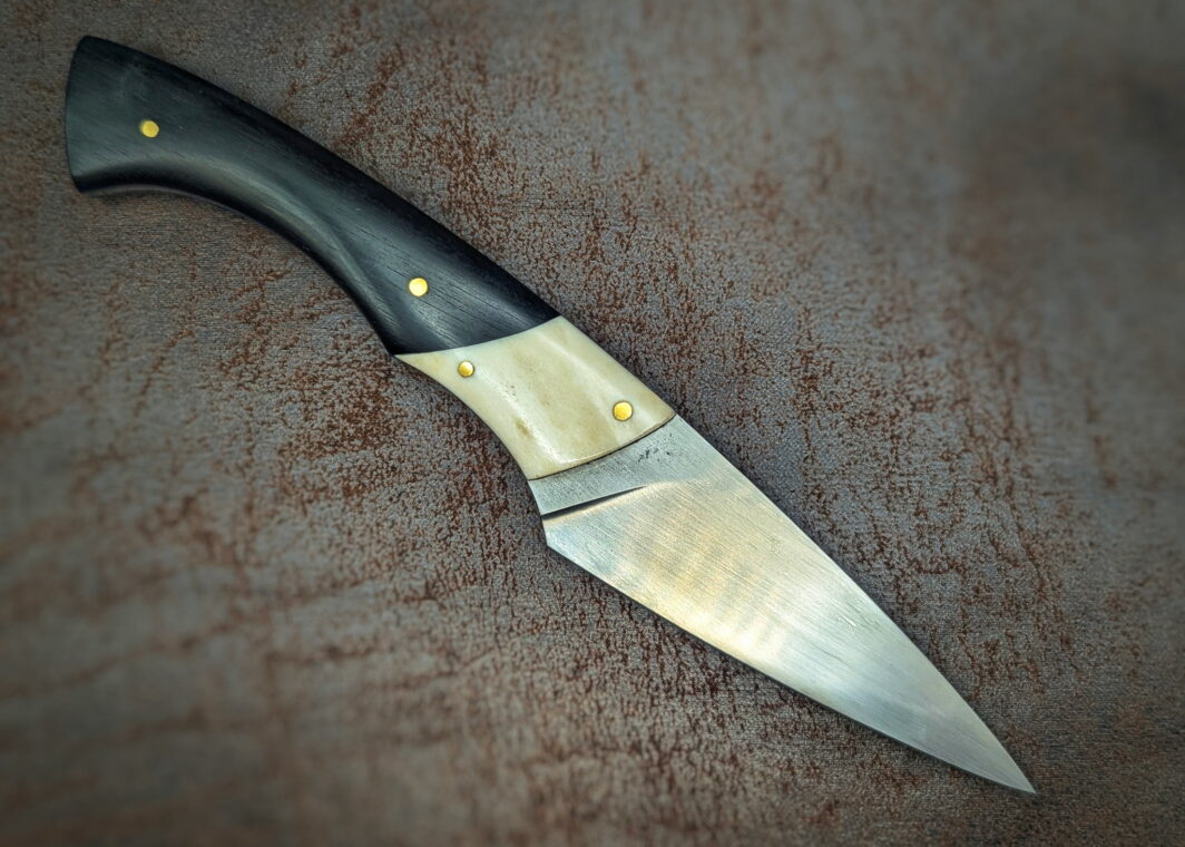 Couteau fixe par l'artisan Dahéna Urli. Vue côté droit. Sa lame est en acier carbone C130 avec finition tirée en long. Son manche est en ébène avec mitre en bois de renne. Couteau artisanal, coutellerie français à Châteauneuf-du-Pape, Vaucluse Coutellerie du Pape