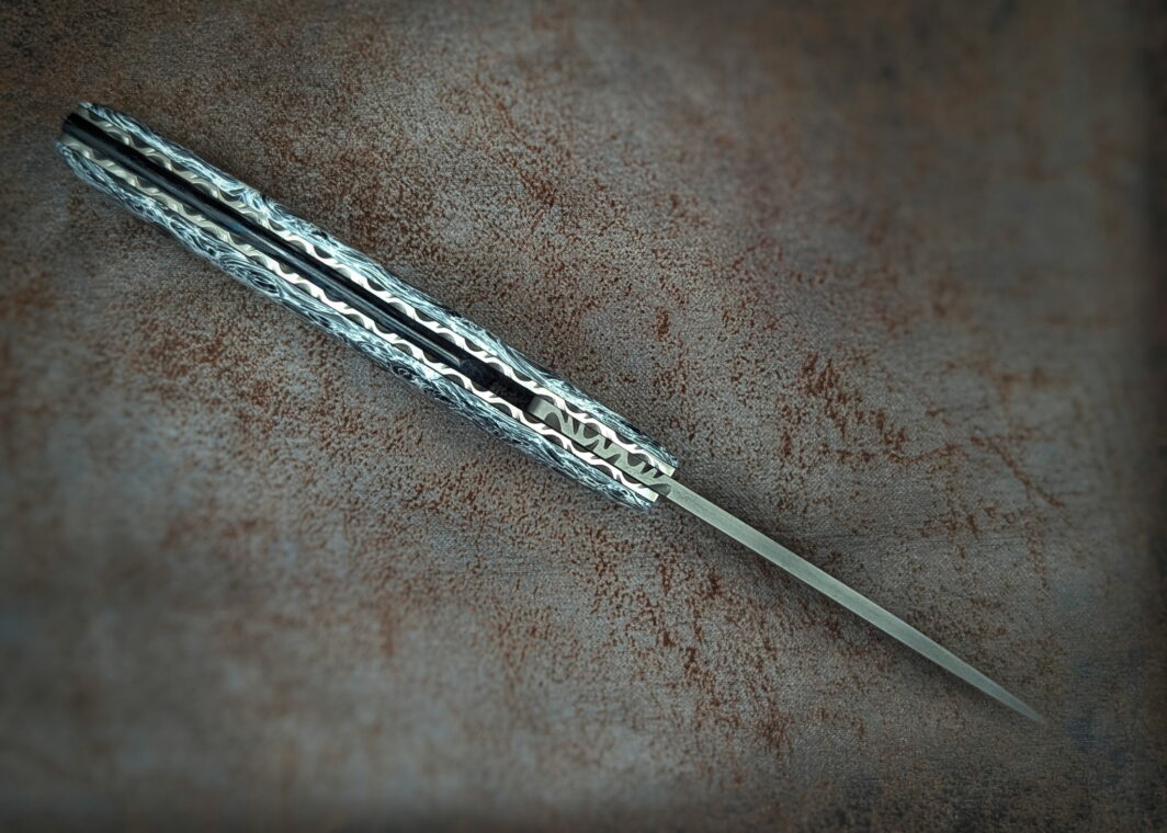 Couteau Piémontais Full Carbone par l'artisan Dahéna Urli. Vue du dessus. On voit la lame et les platines guillochées. Couteau artisanal, coutellerie français à Châteauneuf-du-Pape, Vaucluse Coutellerie du Pape