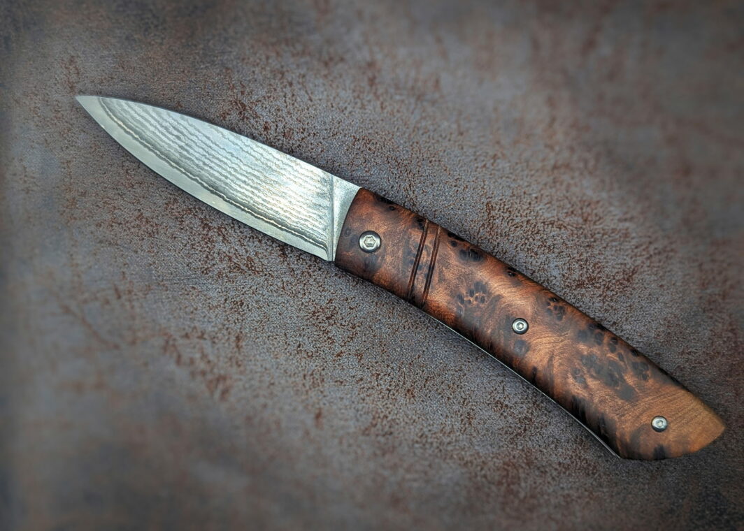 Couteau Piémontais Thuya par l'artisan Dahéna Urli. Position ouverte, côté gauche. Le manche est en Loupe de thuya. La lame est en damas inox. Couteau artisanal, coutellerie français à Châteauneuf-du-Pape, Vaucluse Coutellerie du Pape
