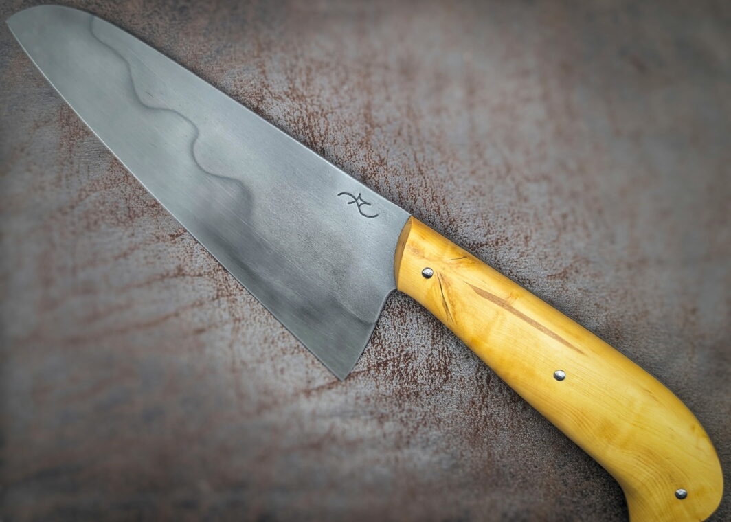 Couteau fixe de cuisine par l'artisan Alban Campagnola. Vue du côté gauche. La lame est en C130 avec une révélation d'une trempe sélective au perchlorure de fer. On voit sur la lame le poinçon d'Alban. Le manche est en Buis. Couteau artisanal, coutellerie français à Châteauneuf-du-Pape, Vaucluse Coutellerie du Pape
