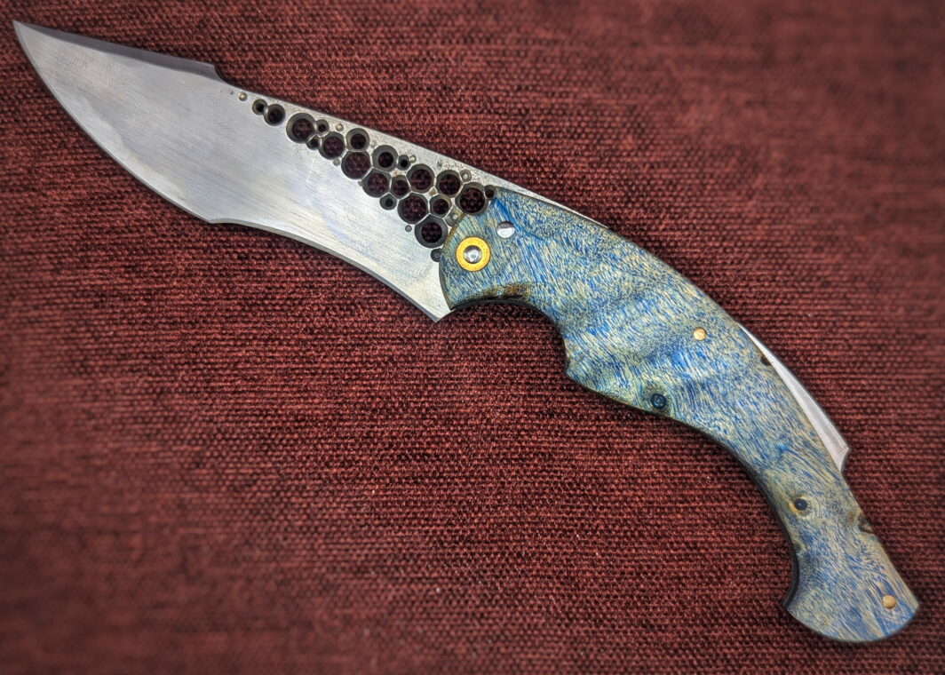 Couteau pliant Amphiptère de l'artisan Dracoforge. Position ouverte, côté gauche. La lame est en Z40 et le manche en Peuplier stabilisé bleu. La fausse pièce dépassant du dessus rappel un univers marin. Couteau artisanal, coutellerie français à Châteauneuf-du-Pape, Vaucluse Coutellerie du Pape