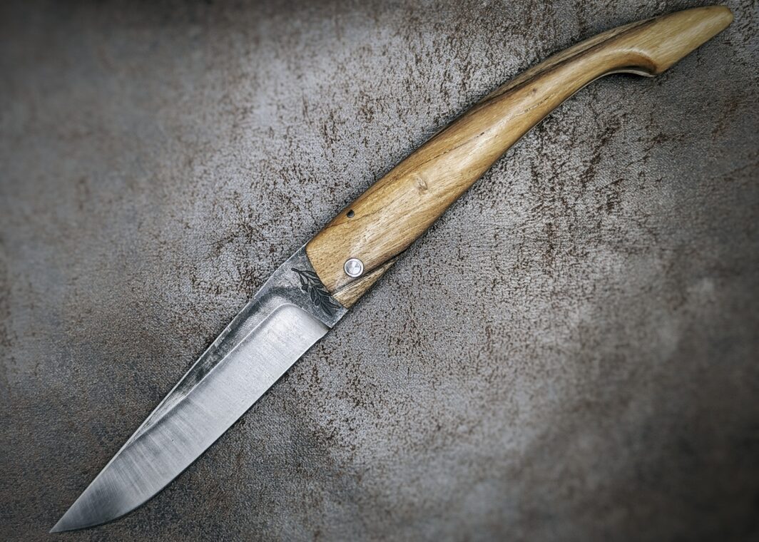 couteau pliant deux clous avec manche en genêt et lame en acier carbone ,position ouverte, coté gauche modéle capulagui