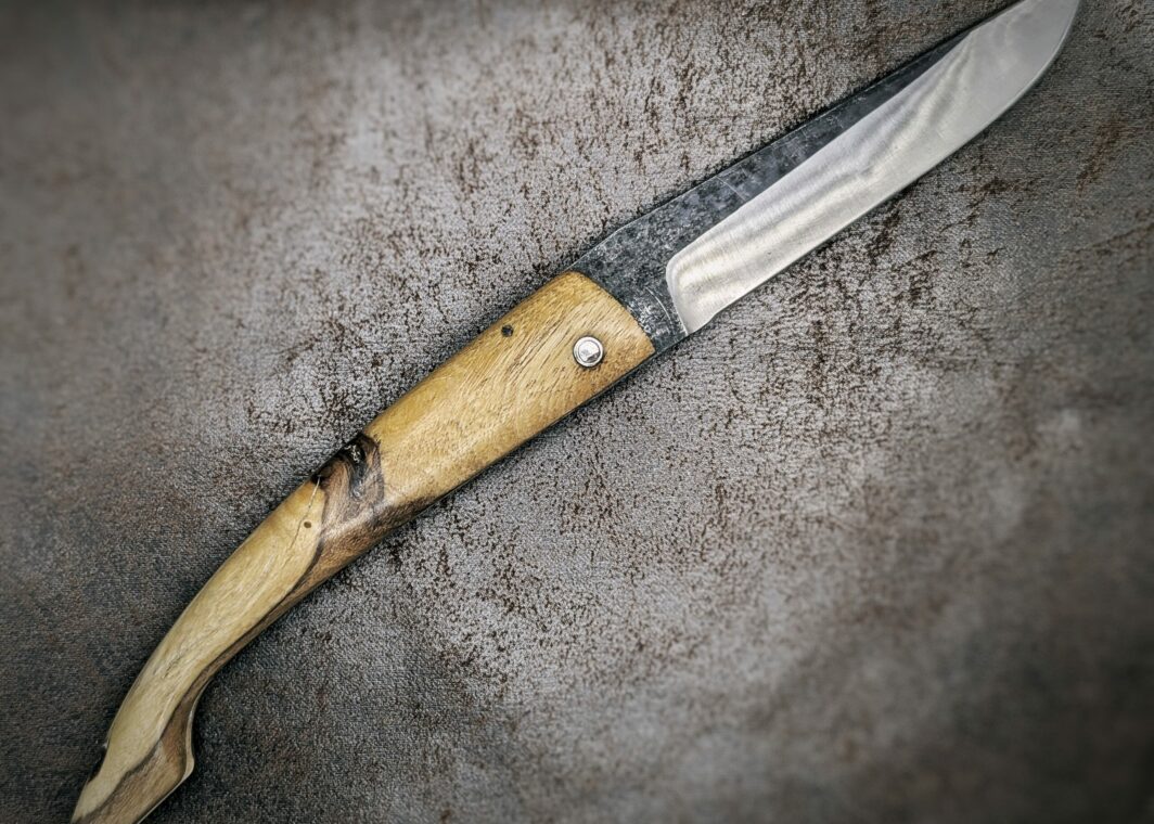 couteau pliant deux clous avec manche en genêt et lame en acier carbone ,position ouverte, coté droit capulagui