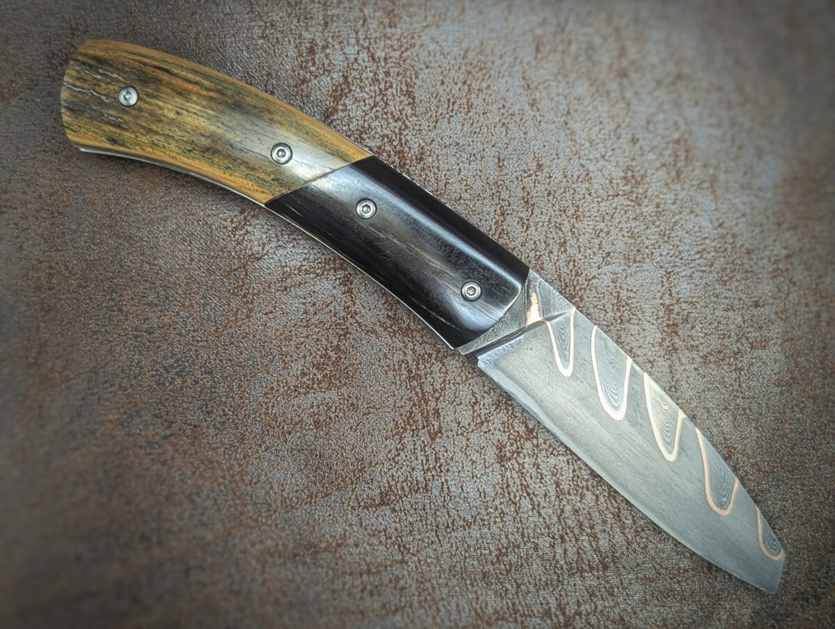Couteau pliant artisanal par Dahéna Urli. Lame en damas cuivre manche en ivoire de mammouth et corne de buffle. Position ouvert, côté droit