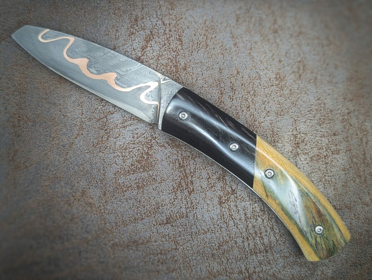 Couteau pliant artisanal par Dahéna Urli. Lame en damas cuivre manche en ivoire de mammouth et corne de buffle. Position ouvert, côté gauche
