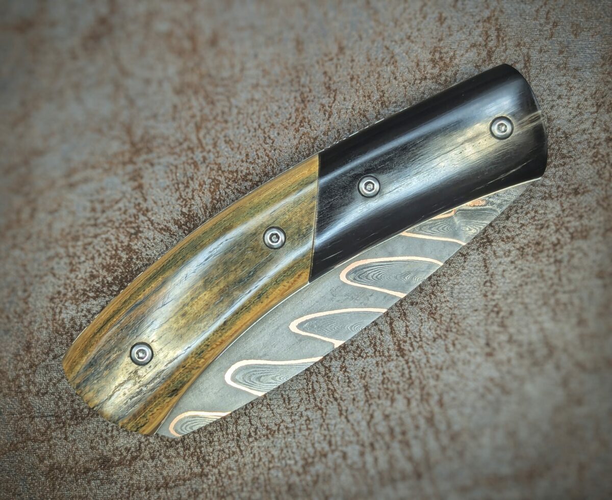 Couteau pliant artisanal par Dahéna Urli. Lame en damas cuivre manche en ivoire de mammouth et corne de buffle. Position fermé, côté droit