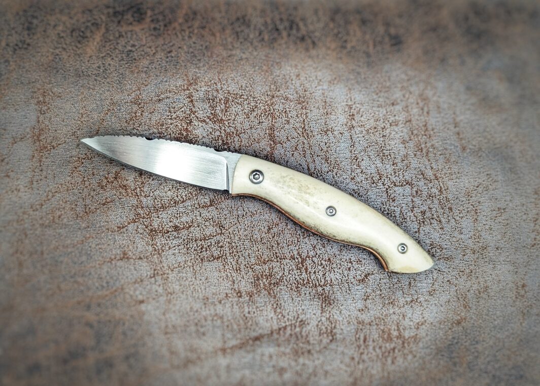 Couteau pliant artisanal par Dahéna Urli. Manche en bois de renne, platines en cuivre et lame en Z40. Position ouverte, côté gauche