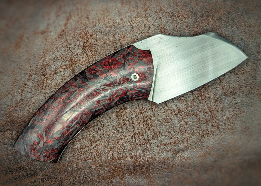 Couteau pliant artisanal par Lou Marius. Lame en acier carbone C130. Manche en fibre de carbone paillette rouge. Position ouverte, vue du côté droit.