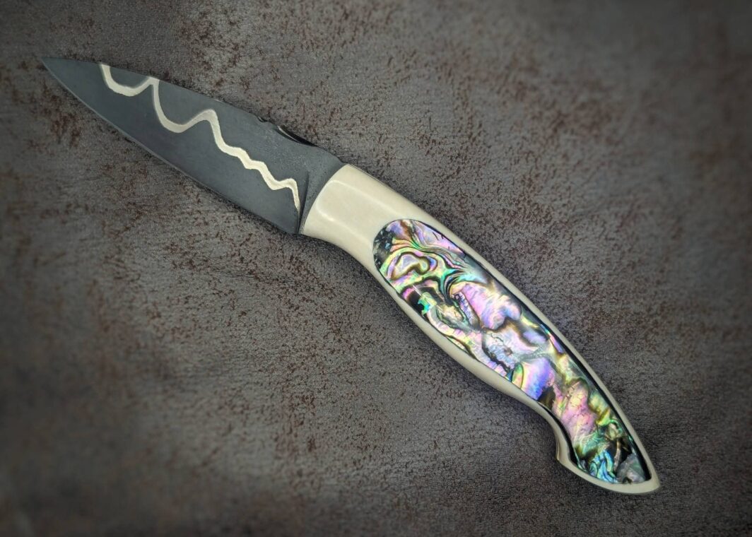 Couteau pliant par l'artisan Dahéna URLI. Lame en acier sandwich carbone, manche en ivoire de mammouth et abalone. Position ouvert, côté gauche