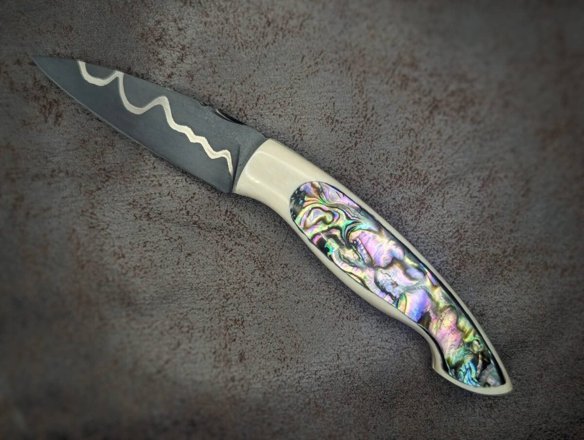 Couteau pliant par l'artisan Dahéna URLI. Lame en acier sandwich carbone, manche en ivoire de mammouth et abalone. Position ouvert, côté gauche