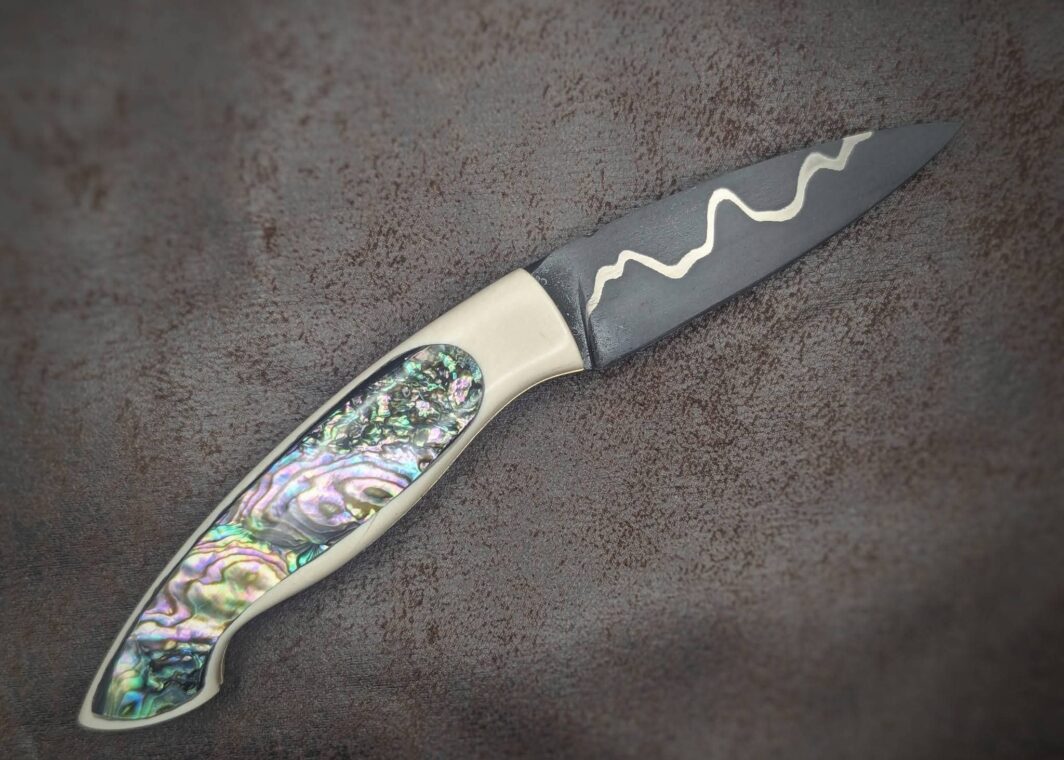 Couteau pliant par l'artisan Dahéna URLI. Lame en acier sandwich carbone, manche en ivoire de mammouth et abalone. Position ouvert, côté droit
