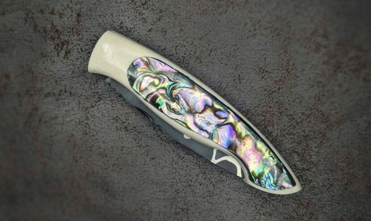 Couteau pliant par l'artisan Dahéna URLI. Lame en acier sandwich carbone, manche en ivoire de mammouth et abalone. Position fermé, côté gauche