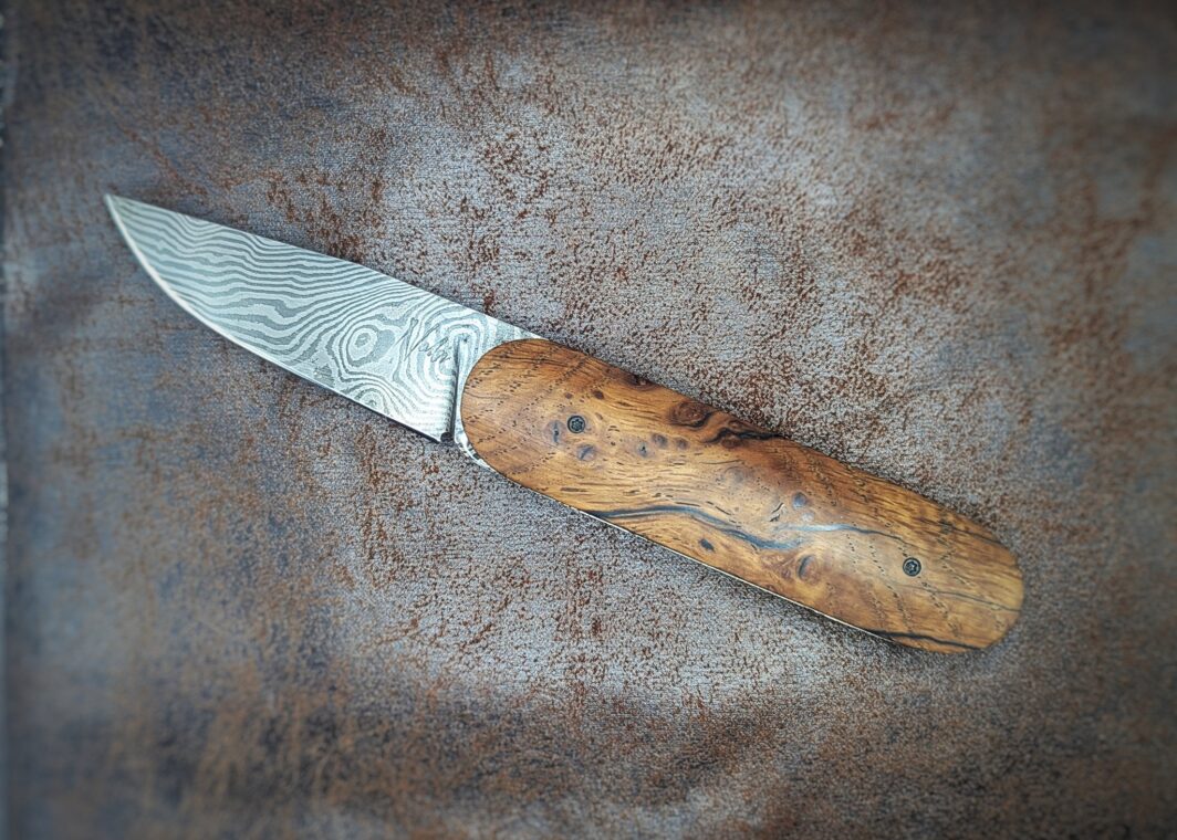 Couteau Le Baldo par l'artisan Noki. Pliant LinerLock FrontFlip. Position ouvert, côté gauche. On voit le poinçon de l'artisan sur la lame damas. Couteau artisanal français à Châteauneuf-du-Pape, Vaucluse Coutellerie du Pape