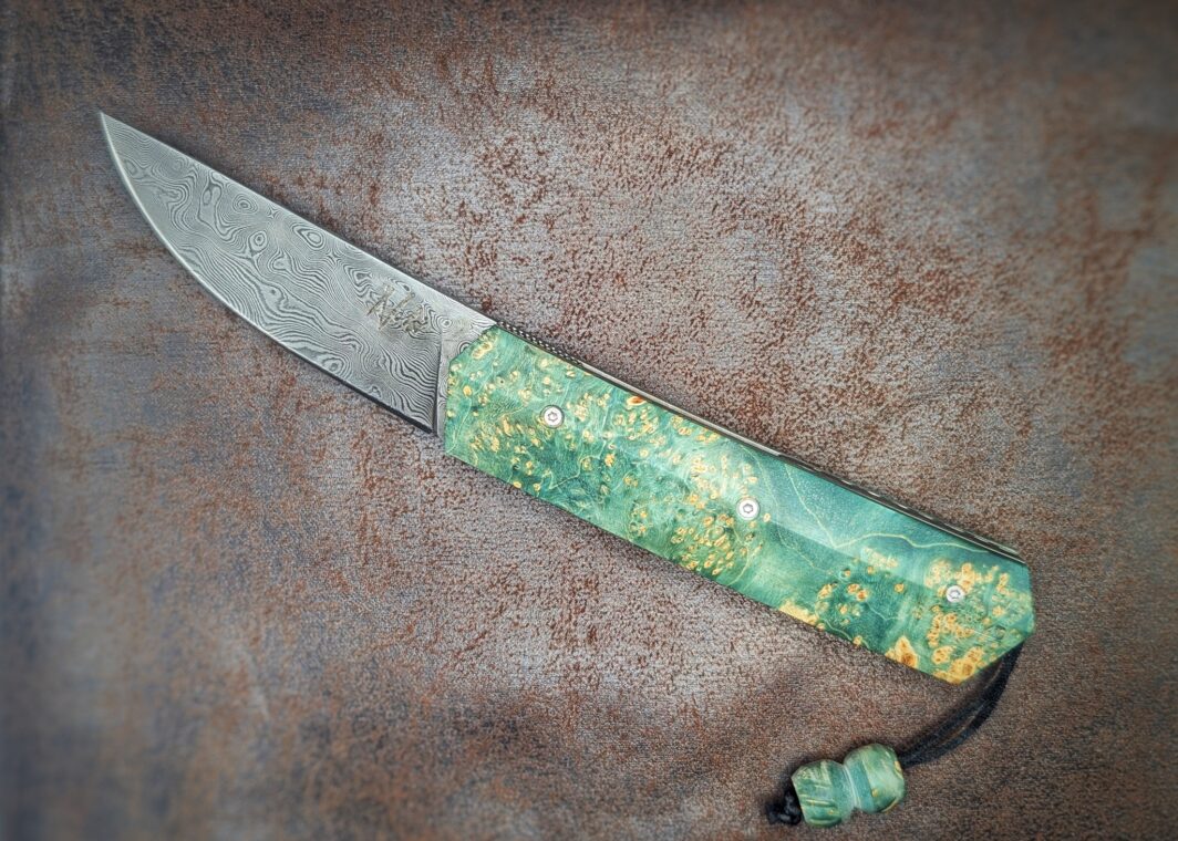 Couteau pliant Liner Lock 'Kiru' de l'artisan Noki. Position ouvert, côté gauche. Lame en damas 208 couches.. On voit le poinçon de l'artisan sur la lame. Avec étui en cuir noir. Couteau artisanal français à Châteauneuf-du-Pape, Vaucluse Coutellerie du Pape