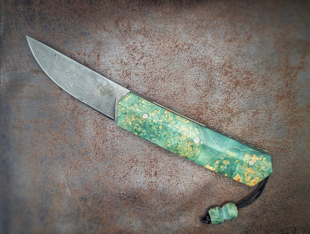 Couteau pliant Liner Lock 'Kiru' de l'artisan Noki. Position ouvert, côté gauche. Lame en damas 208 couches.. On voit le poinçon de l'artisan sur la lame. Avec étui en cuir noir. Couteau artisanal français à Châteauneuf-du-Pape, Vaucluse Coutellerie du Pape