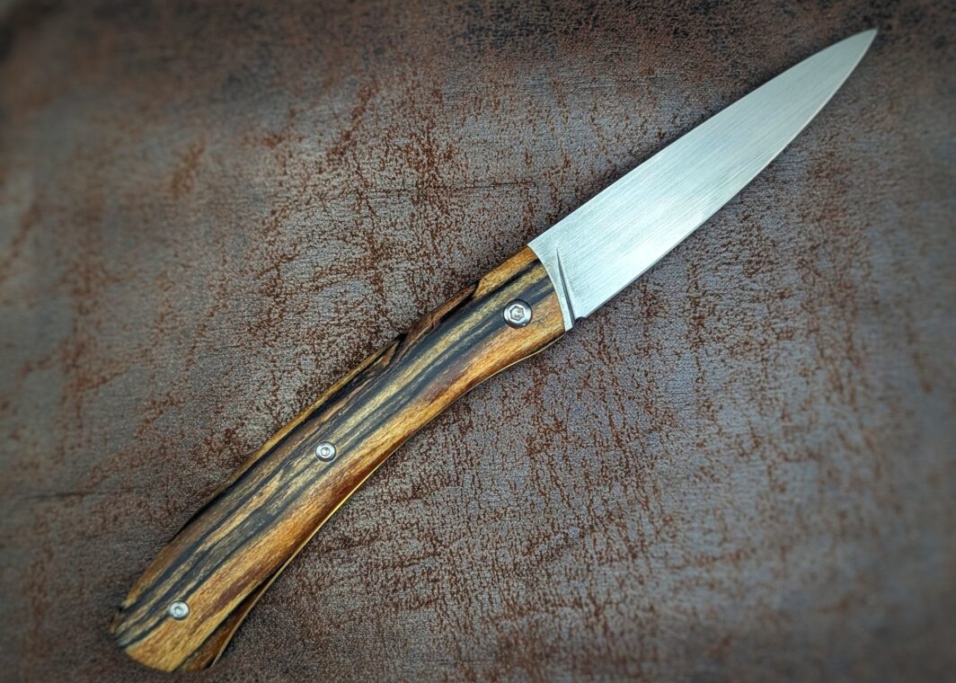 Couteau cran forcé artisanal par Dahéna URLI. Lame en inox Z40 et manche en hêtre. Platines en laiton avec guillochage. Position ouvert, côté droit